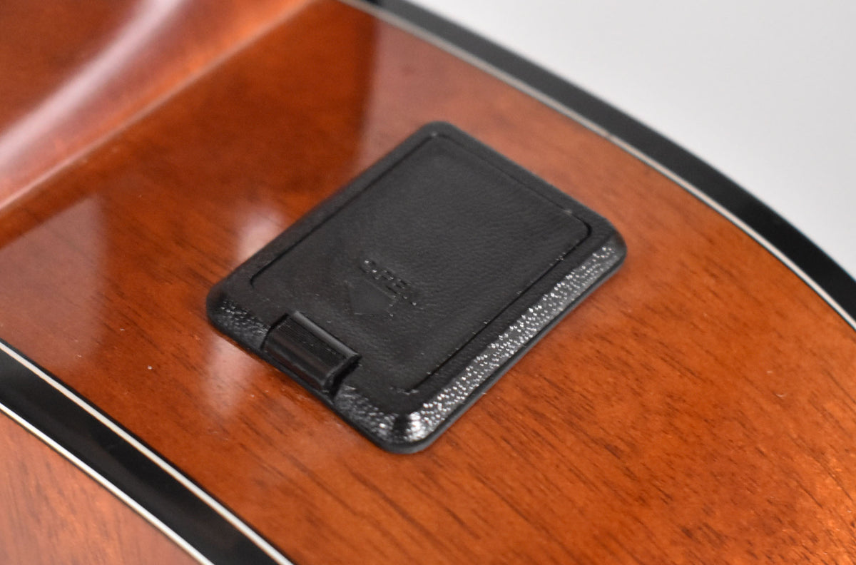 Close-up of the guitar's glossy reddish-brown body, showing a black rectangular battery compartment with a textured edge.
