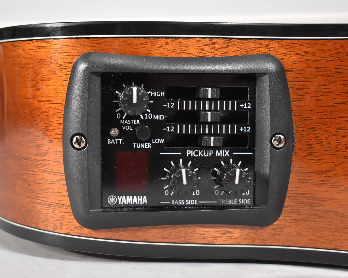 Close-up of the guitar's reddish-brown wood side, showing the black preamp control panel with knobs, sliders, and a tuner display.