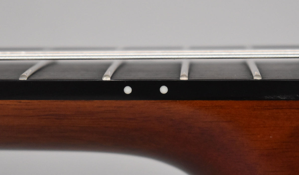 Close-up of the guitar's dark fretboard and brown neck, showing two white side dot markers and four frets with nylon strings.