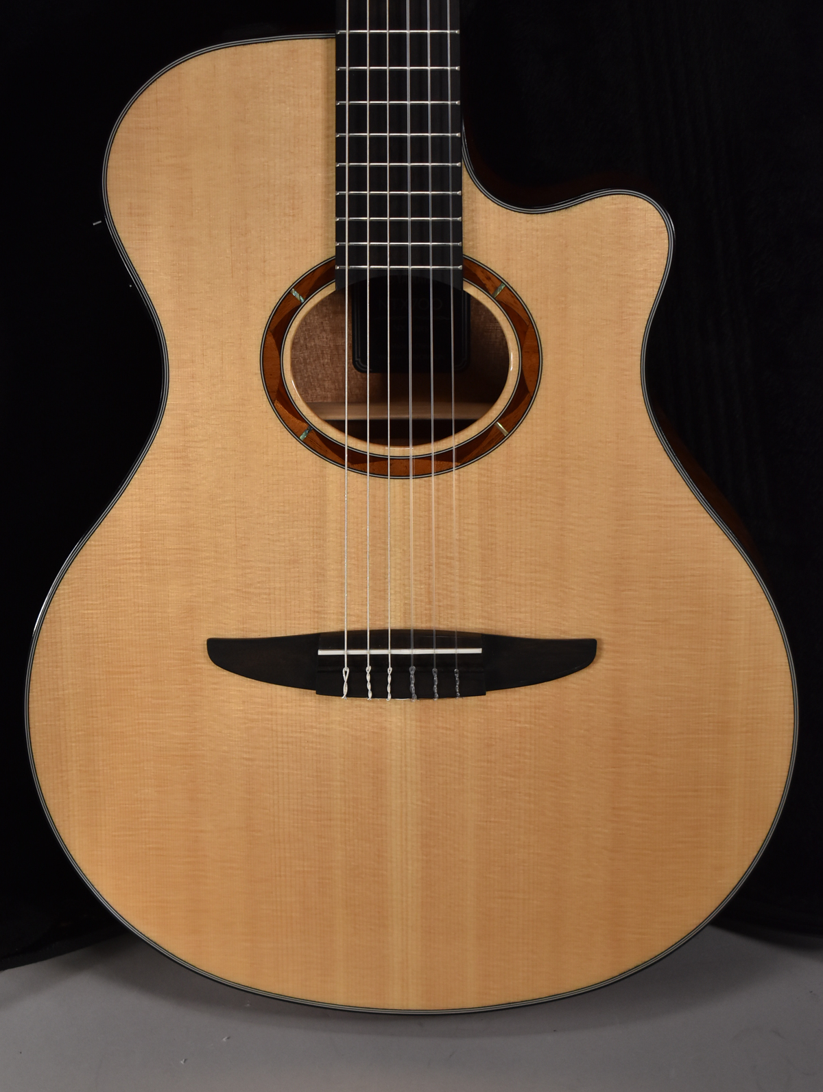 Full front view of a light-colored classical guitar with a cutaway, dark fretboard, and a black bridge with white strings.
