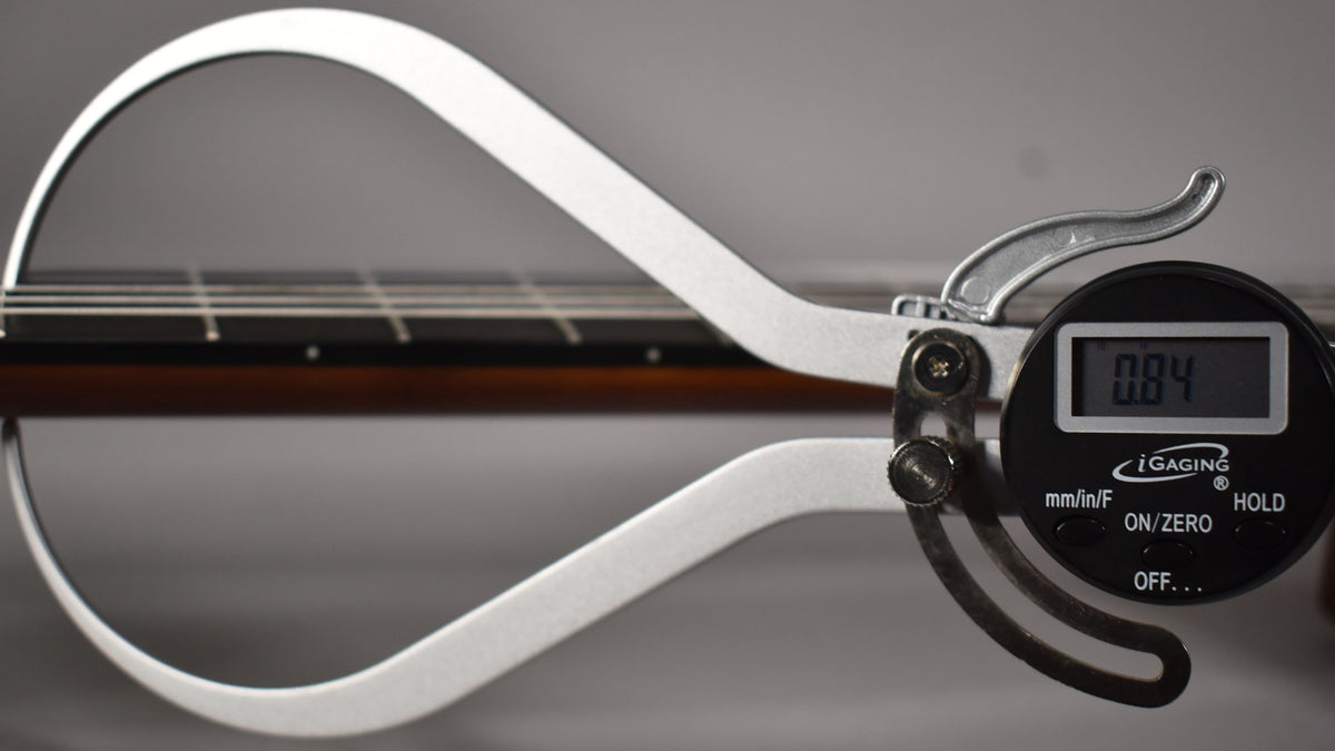 A digital caliper measures the guitar's dark brown neck and fretboard, showing a reading of 0.84.