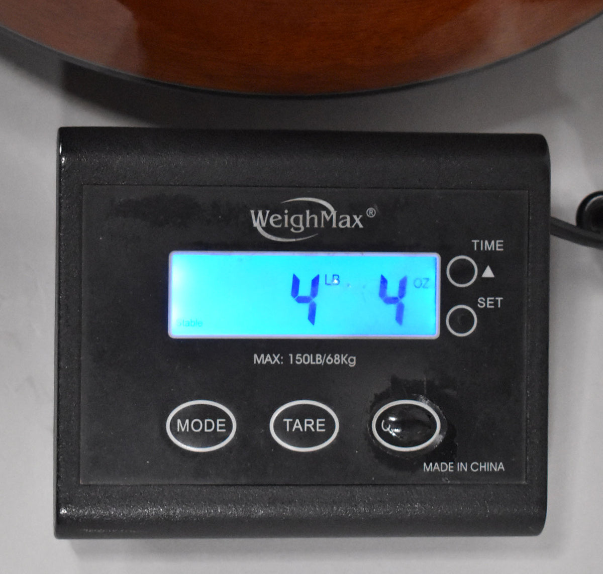 A black digital scale displays "4 LB 4 OZ" in bright blue, with the guitar's lower bout visible above.