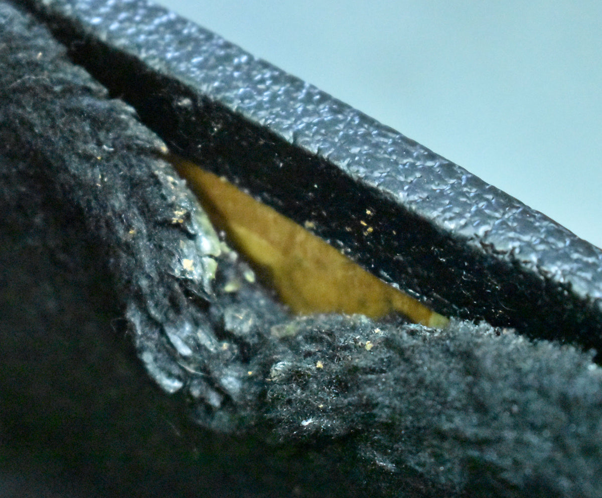 Close-up of the hard shell case's black textured exterior and worn, peeling black plush interior lining, revealing the yellow foam underneath.