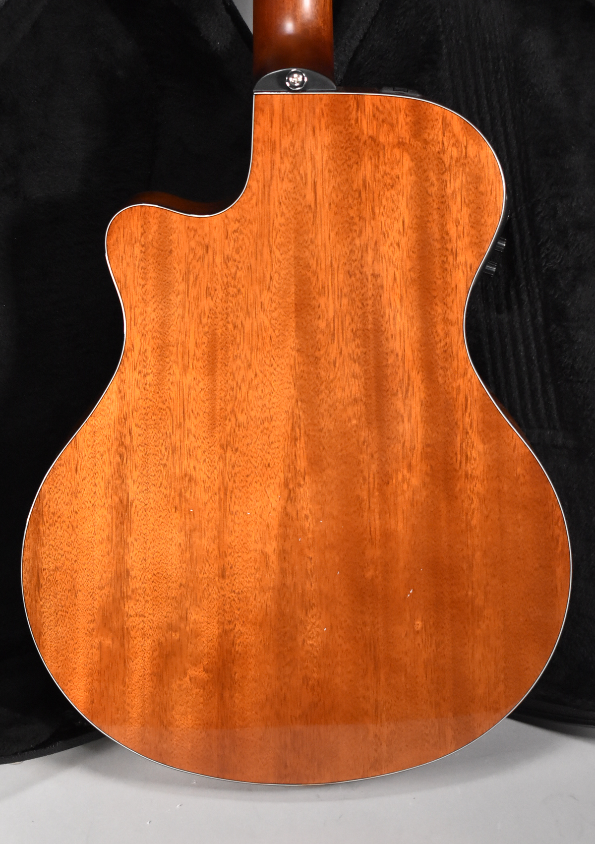 The back of a classical guitar, showing its reddish-brown wood grain, a cutaway, and a strap button at the neck joint.