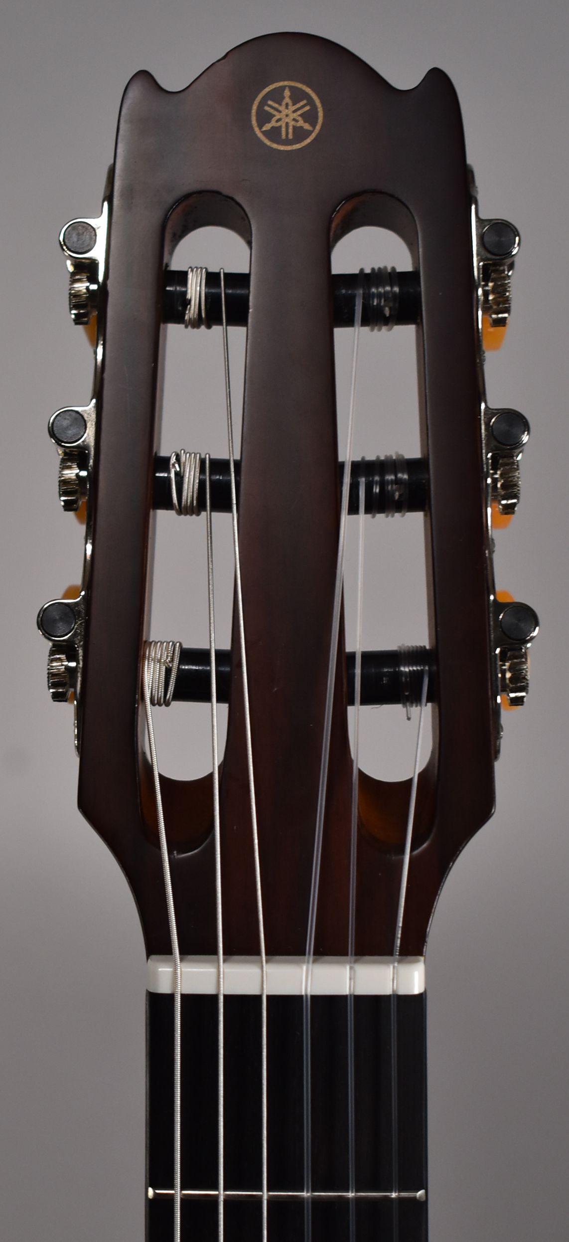 Close-up of the dark brown headstock, showing the gold-colored tuning machine buttons and a gold emblem at the top.