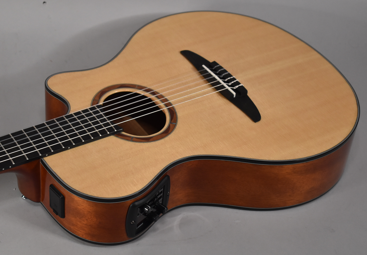 The classical guitar's light wood top and dark sides are angled from the lower left, showing the soundhole and preamp controls.