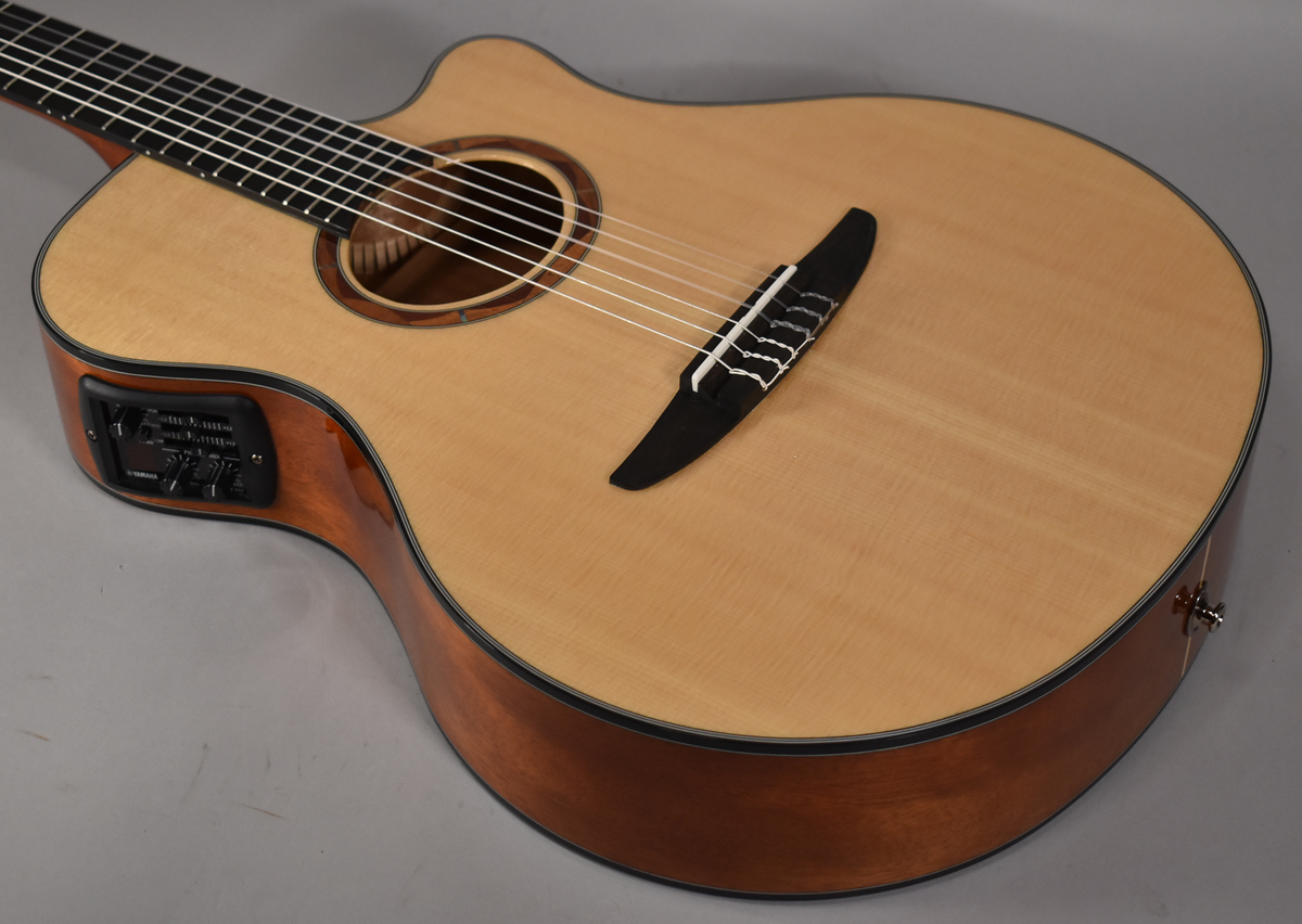 The classical guitar's light wood top and dark sides are angled from the lower left, showing the preamp controls and cutaway.