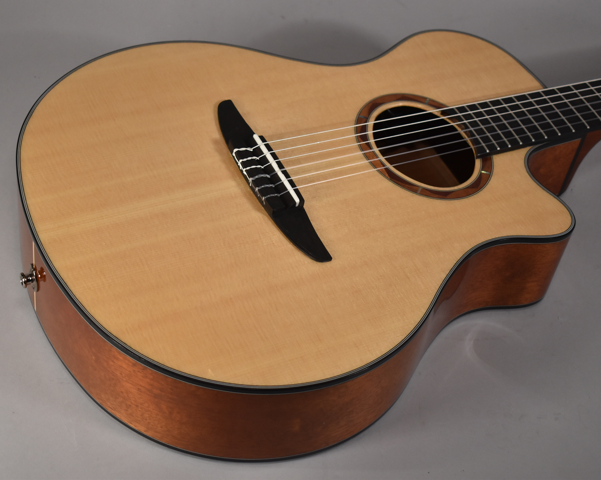 The classical guitar's light wood top and dark wood sides are visible from the upper bout, with a black bridge and rosette.