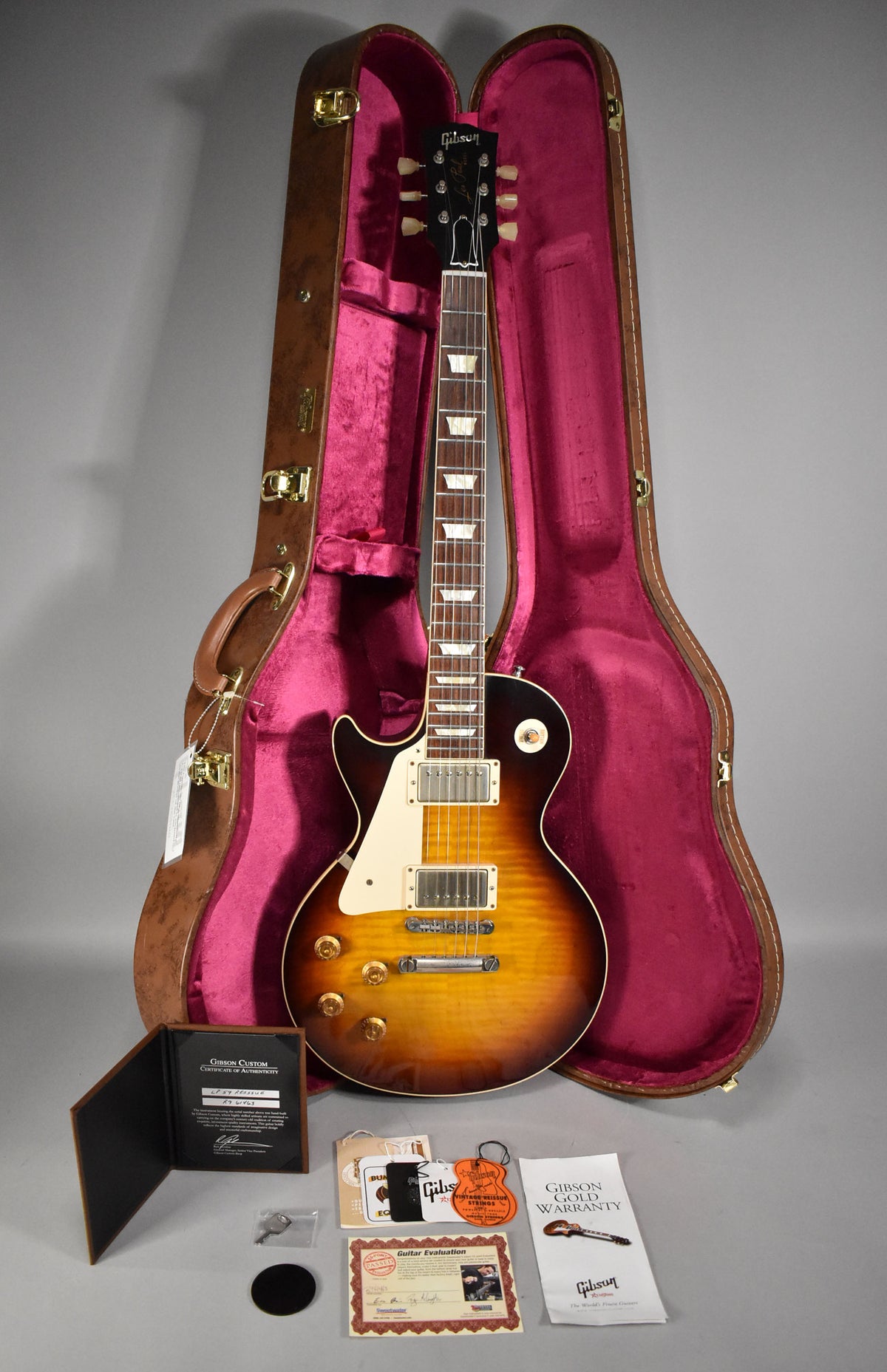A left-handed Gibson Les Paul in a brown case with red velvet lining, with paperwork, a key, and a black circular disc.