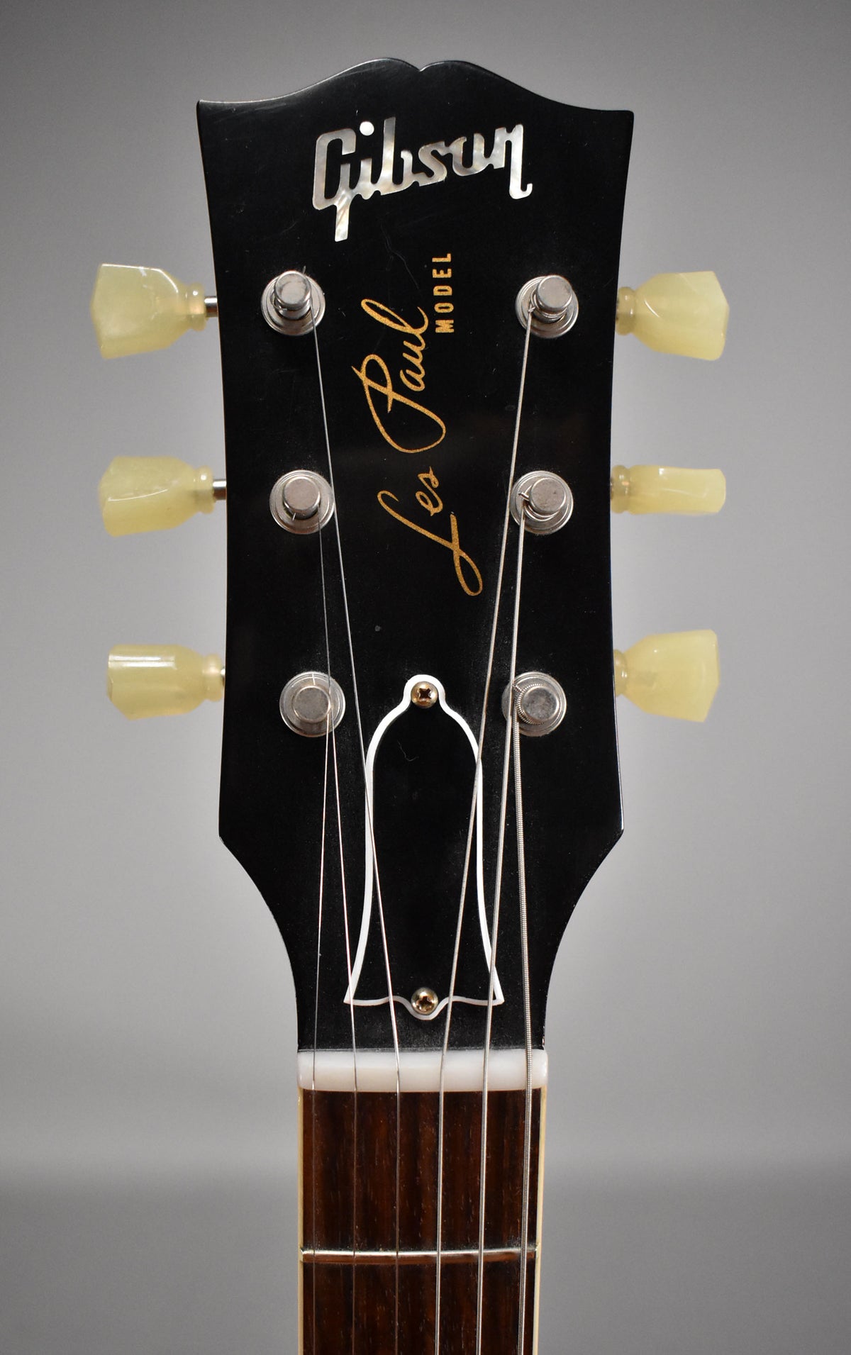 Close-up of a black headstock with six cream-colored tuners, a white truss rod cover, and the top of a dark fretboard.