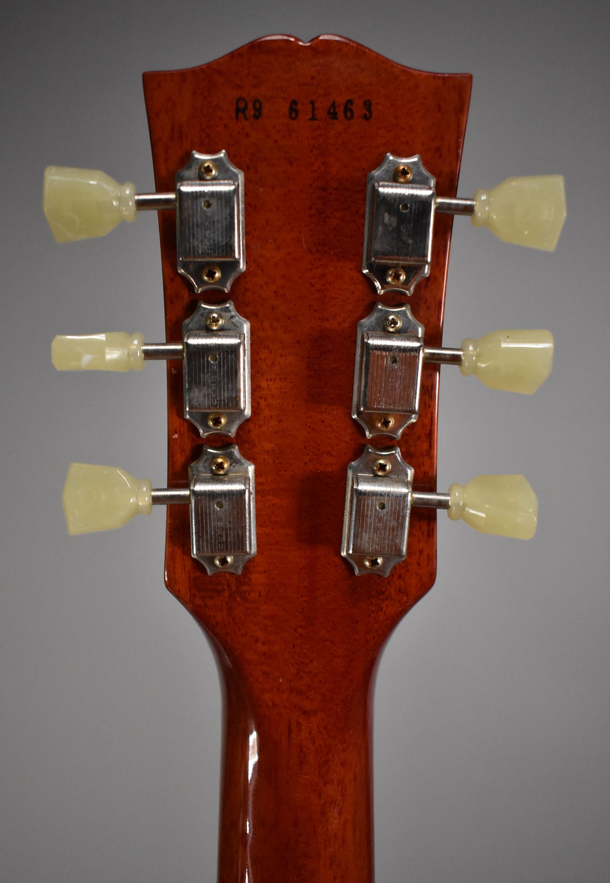 Rear view of the guitar's headstock and upper neck, showing six cream-colored tuning pegs and chrome tuners on a faded tobacco finish.