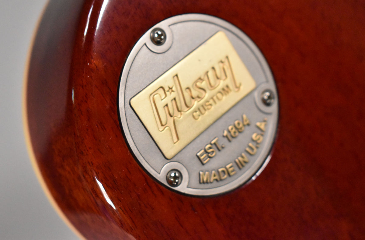 Close-up of the guitar's faded tobacco finish, showing a round, brushed metal backplate with a raised gold rectangular logo.