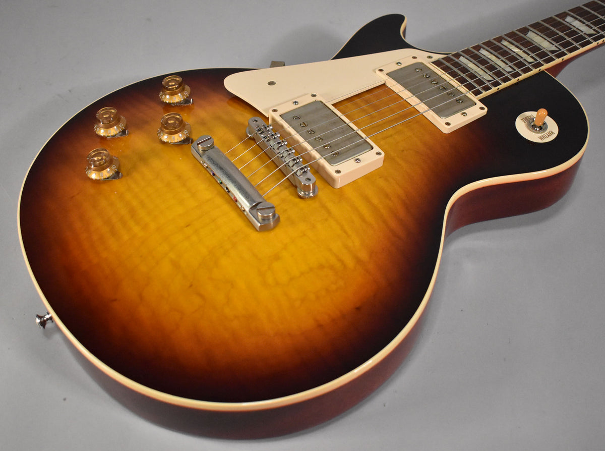 The guitar's body, angled from the lower left, shows a faded tobacco burst finish with visible wood grain and four amber control knobs.