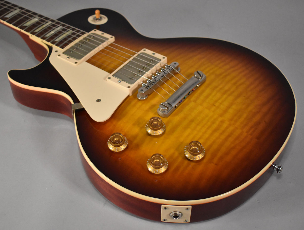 Left-handed Les Paul, faded tobacco burst, angled from the neck to the lower bout, showing four amber control knobs and output jack.