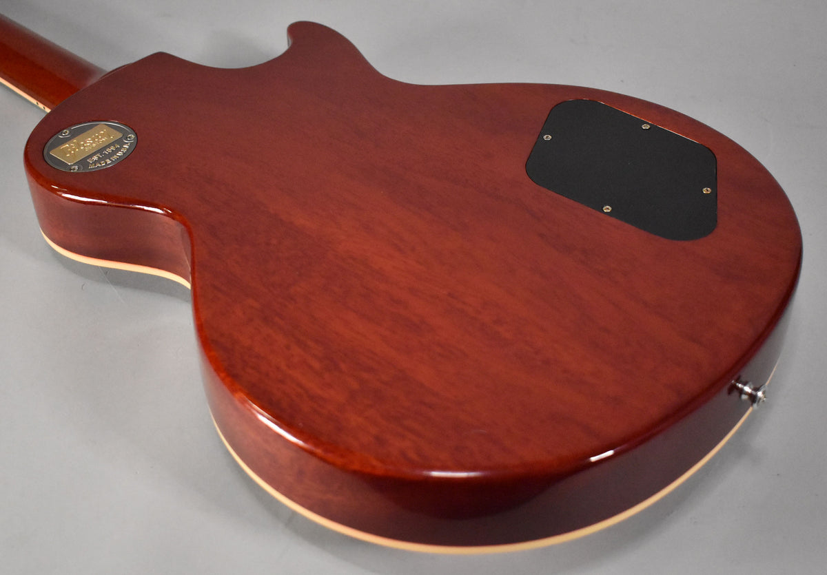 The guitar's back, in faded tobacco, shows a control cavity cover, output jack, and a gold medallion on the neck heel.