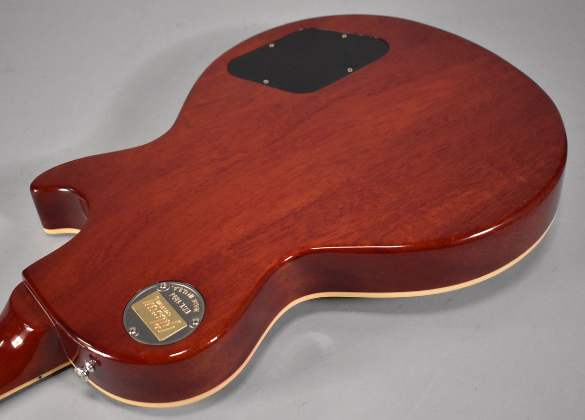 The back of a faded tobacco Les Paul shows a control cavity cover, a circular metal plate, and cream binding.