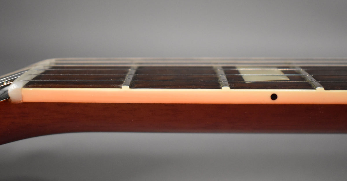 Close-up of the guitar's fretboard from the side, showing dark frets, cream binding, and a single black side dot marker.