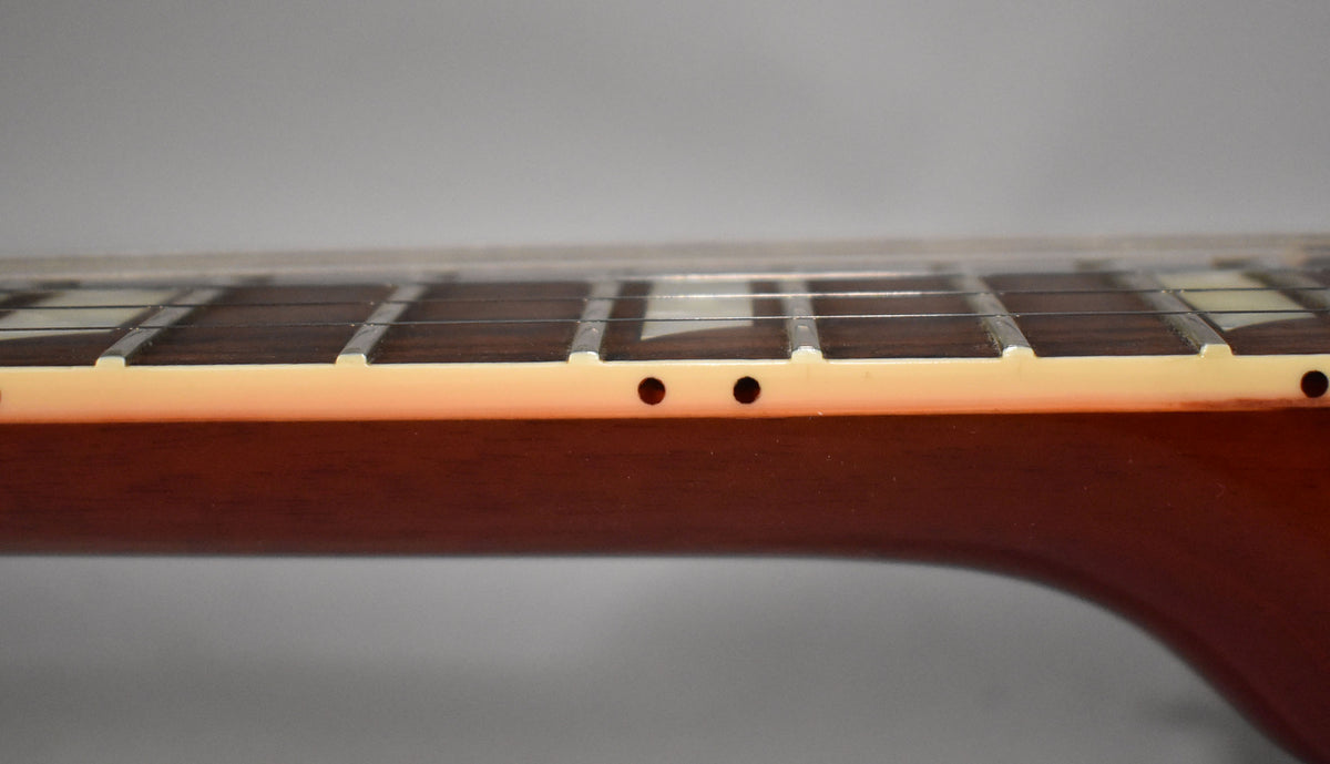 The guitar's dark brown neck and fretboard are viewed from the side, showing two black dot markers on the cream binding.