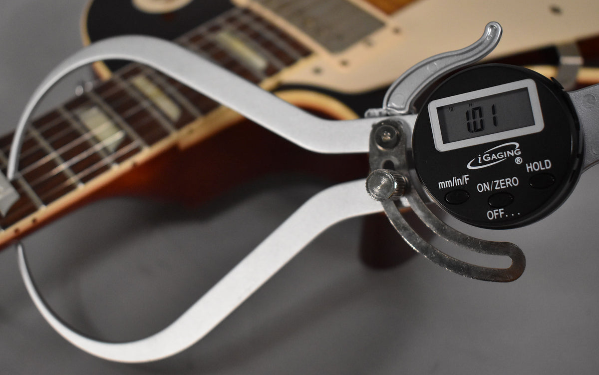 A digital caliper measures the nut width of the Les Paul's dark rosewood fretboard with trapezoid inlays, displaying "1.01".