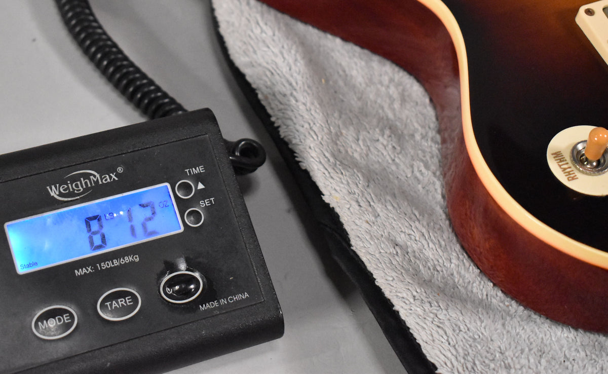 Close-up of the guitar's lower bout on a scale, showing 8 lb 12 oz, faded tobacco finish, cream binding, and the "RHYTHM" pickup selector.