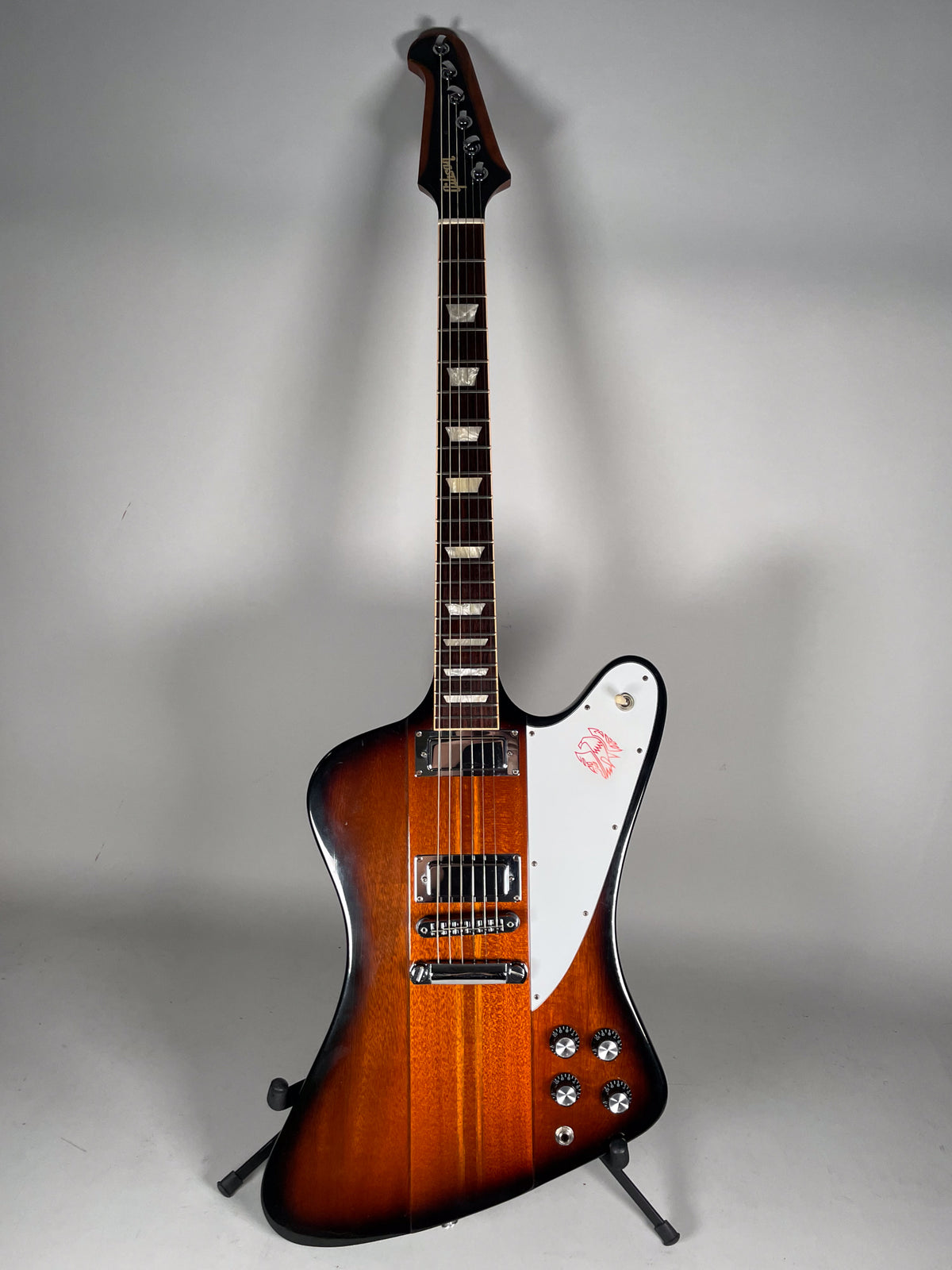 Full-length view of a sunburst Firebird with a white pickguard featuring a red bird graphic, chrome hardware, and four black control knobs.