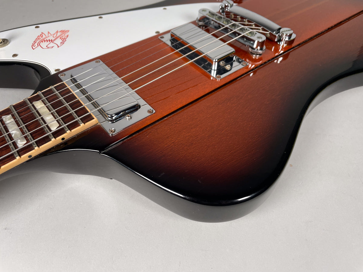 Close-up of the guitar body's lower bout, showing the sunburst finish, chrome humbuckers, and white pickguard with red graphic.