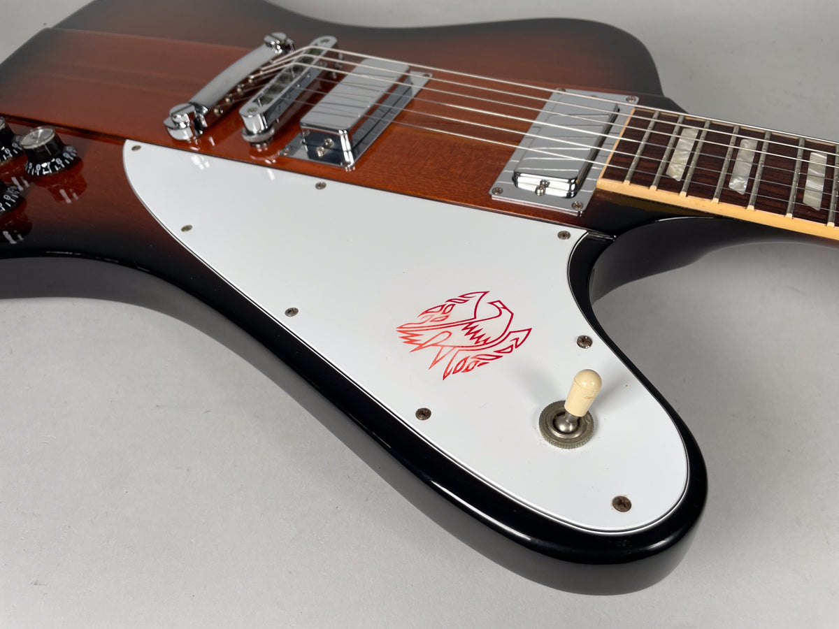Upper body of a sunburst electric guitar, showing a large white pickguard with a red bird graphic and a cream toggle switch.