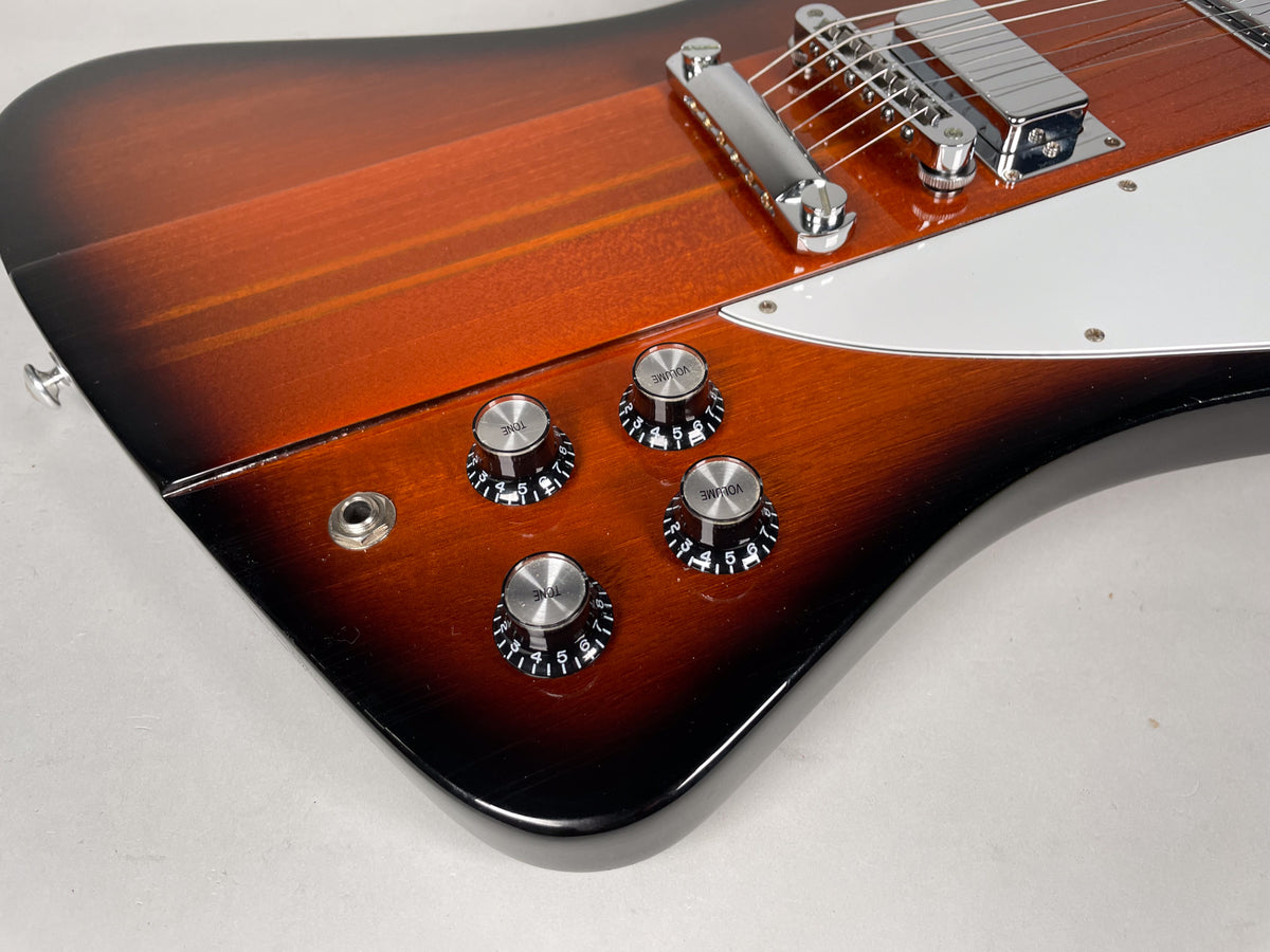Close-up of the Firebird's lower body, showing the sunburst finish, four chrome knobs, output jack, and part of the white pickguard.