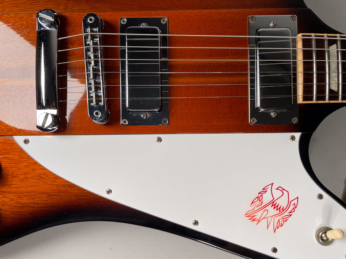 Close-up of the guitar's sunburst body, showing the chrome bridge, two humbucker pickups, and a white pickguard with a red bird graphic.