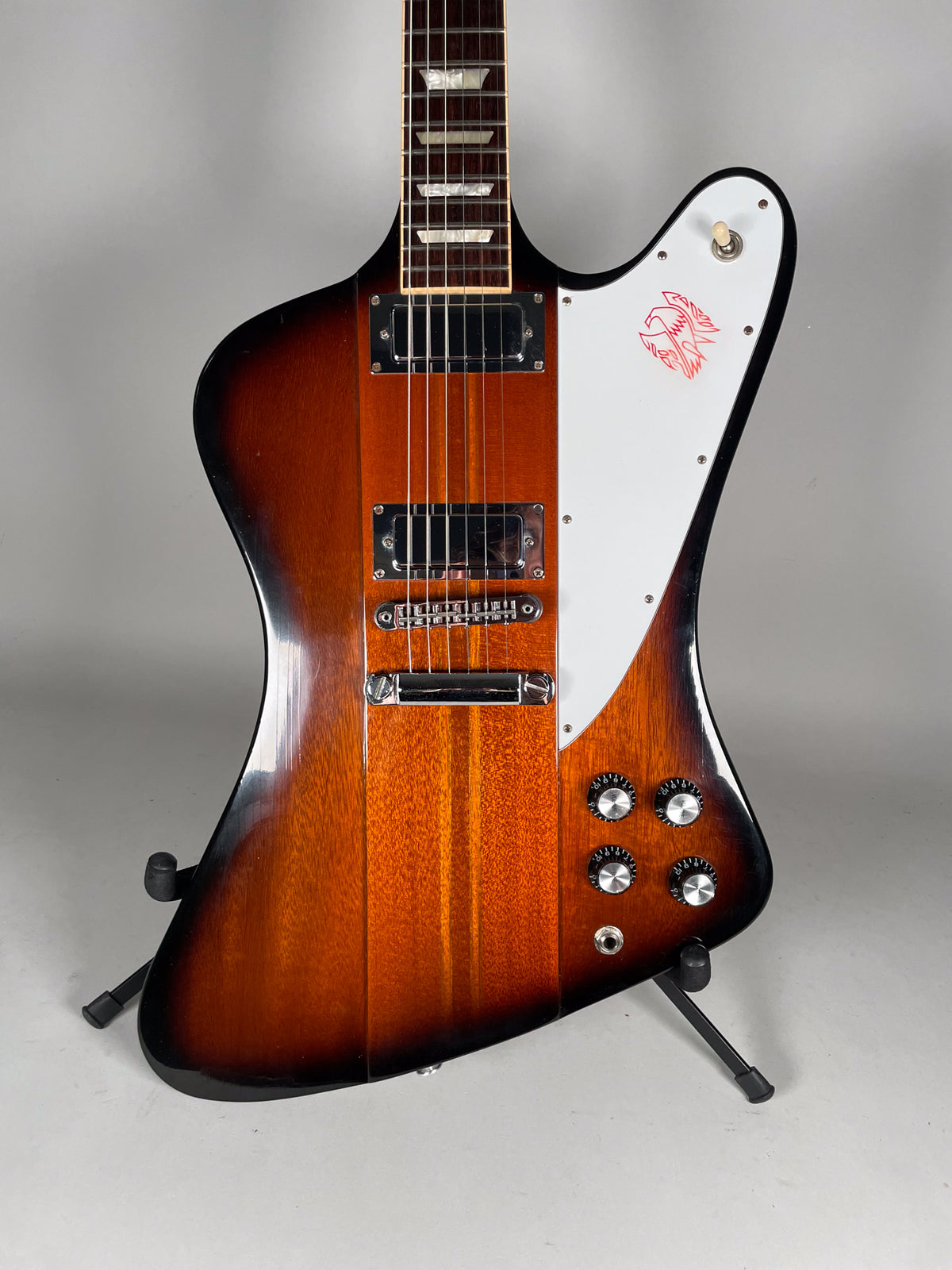 Full-body shot of a sunburst Firebird with a white pickguard featuring a red bird graphic, chrome hardware, and four control knobs.