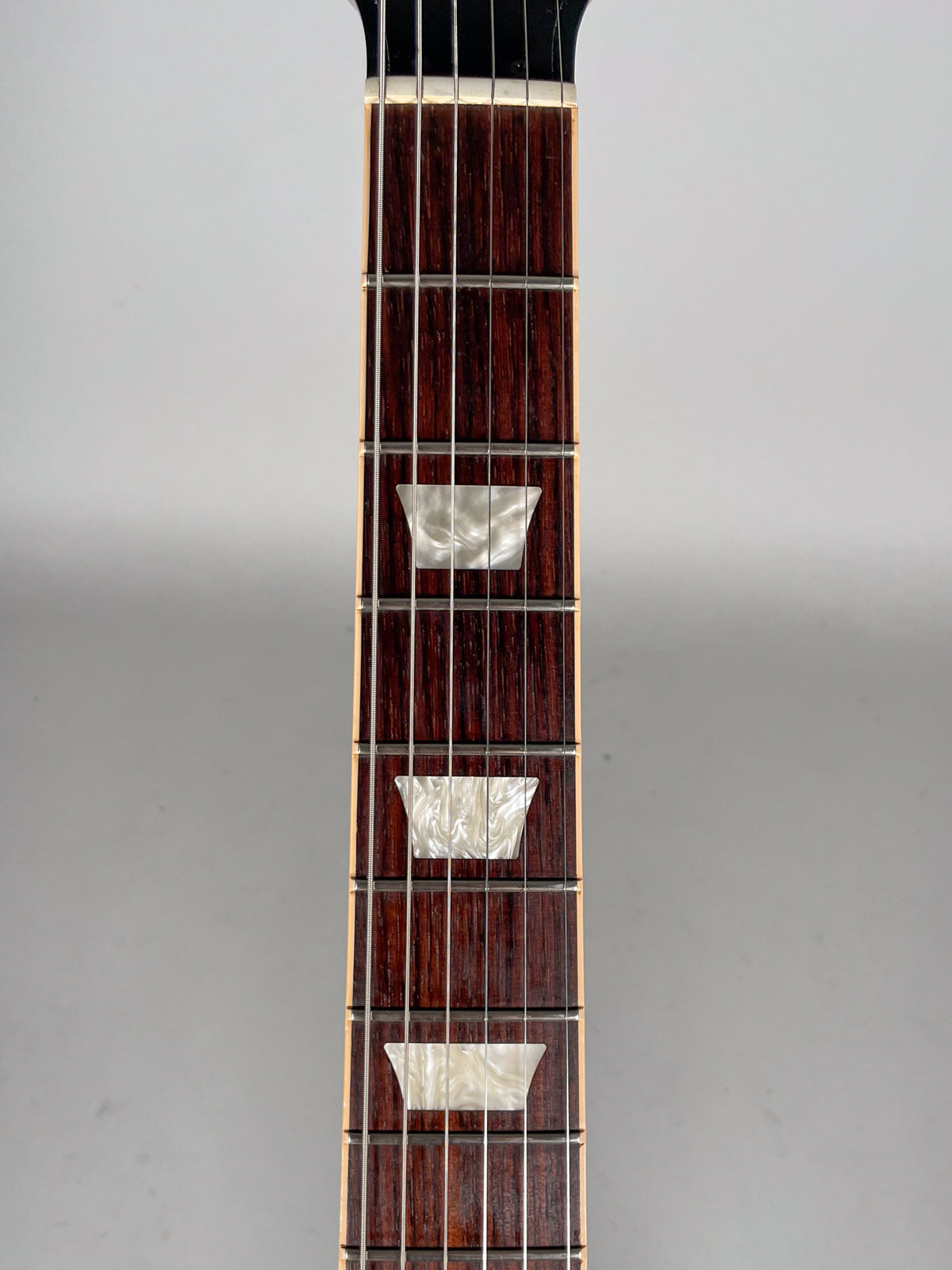 Close-up of the dark rosewood fretboard with trapezoid mother-of-pearl inlays, showing frets 5 through 9.