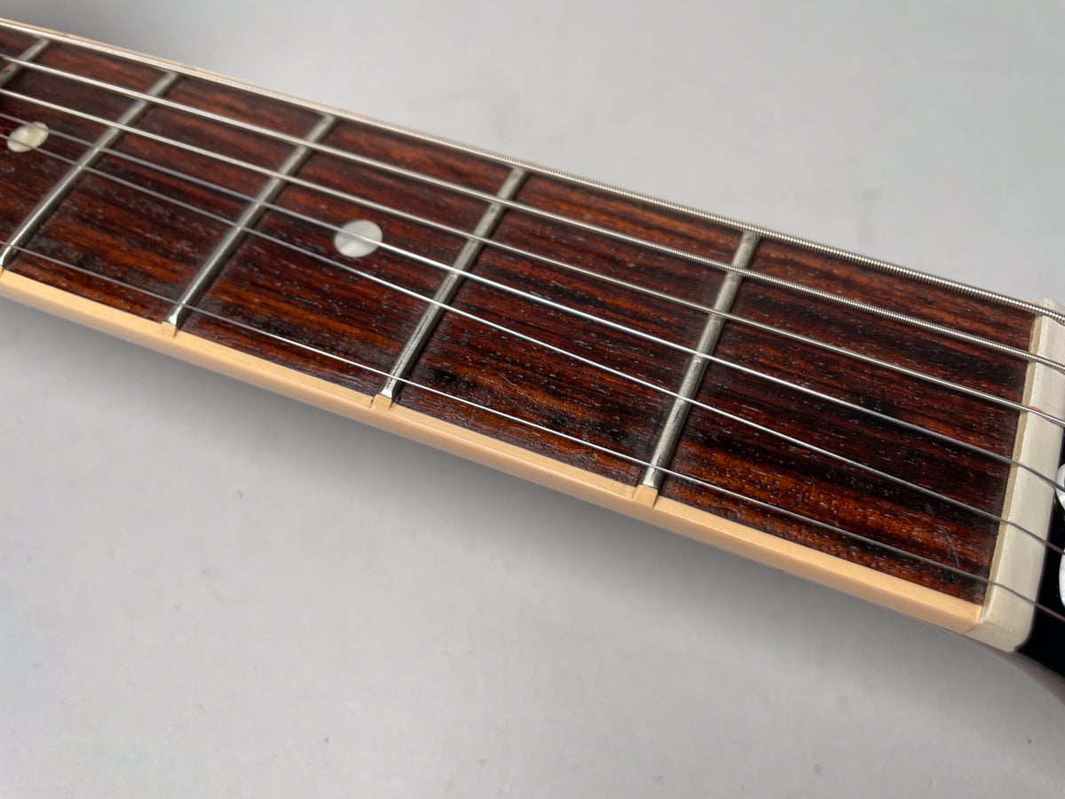 Close-up of the dark rosewood fretboard with light cream binding, showing frets and dot inlays, and the white nut.