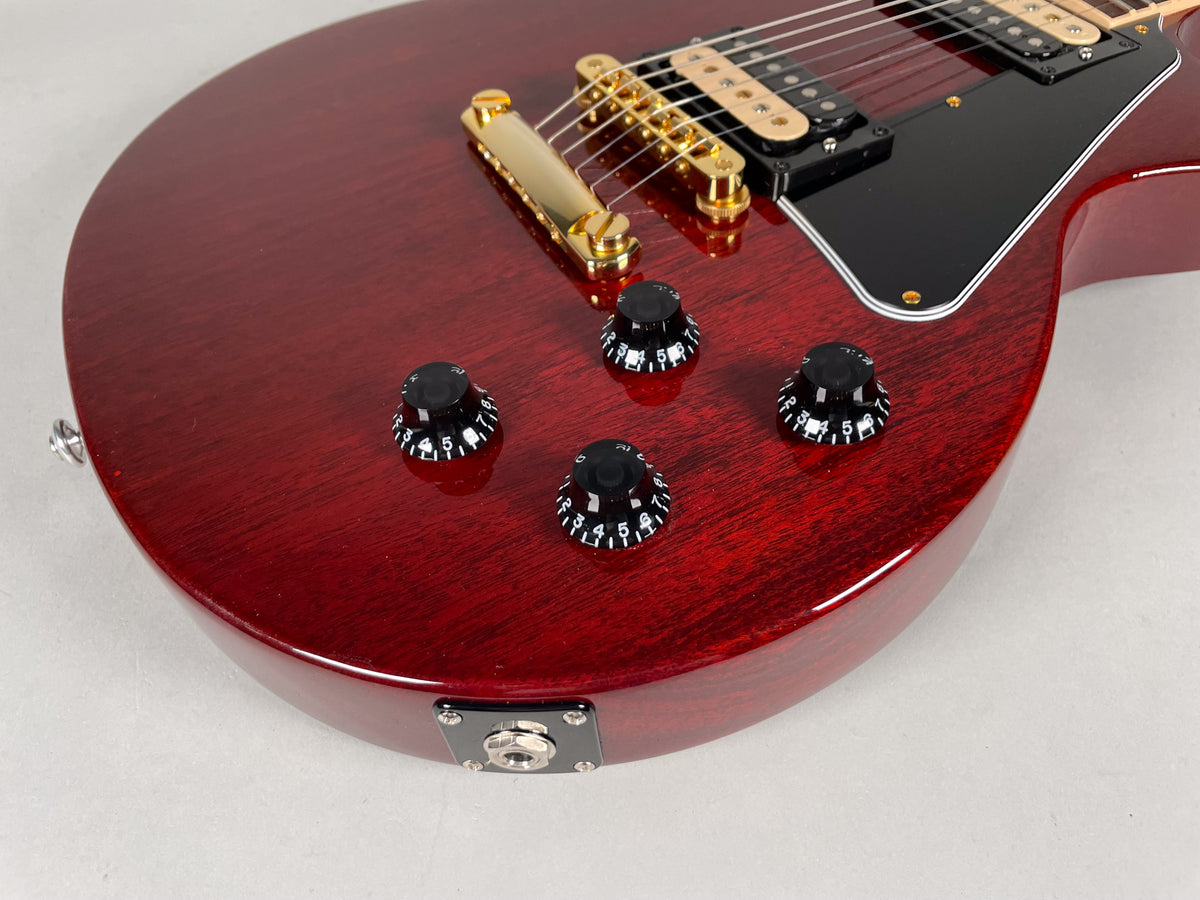 Close-up of the cherry-finished body, showing four black control knobs, gold bridge, black pickguard, and output jack.