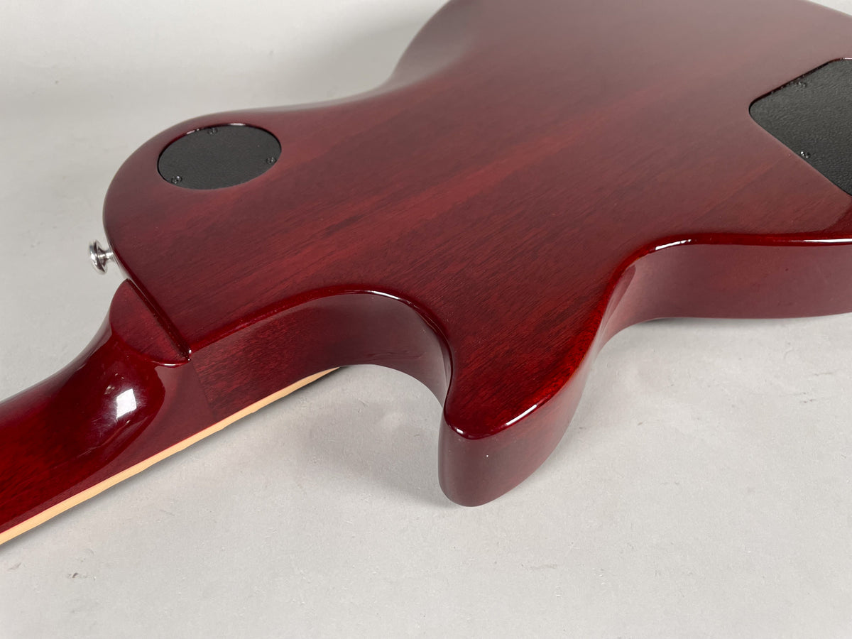 The guitar's cherry red body and neck heel are shown from the back, with a black control cavity cover and strap button visible.