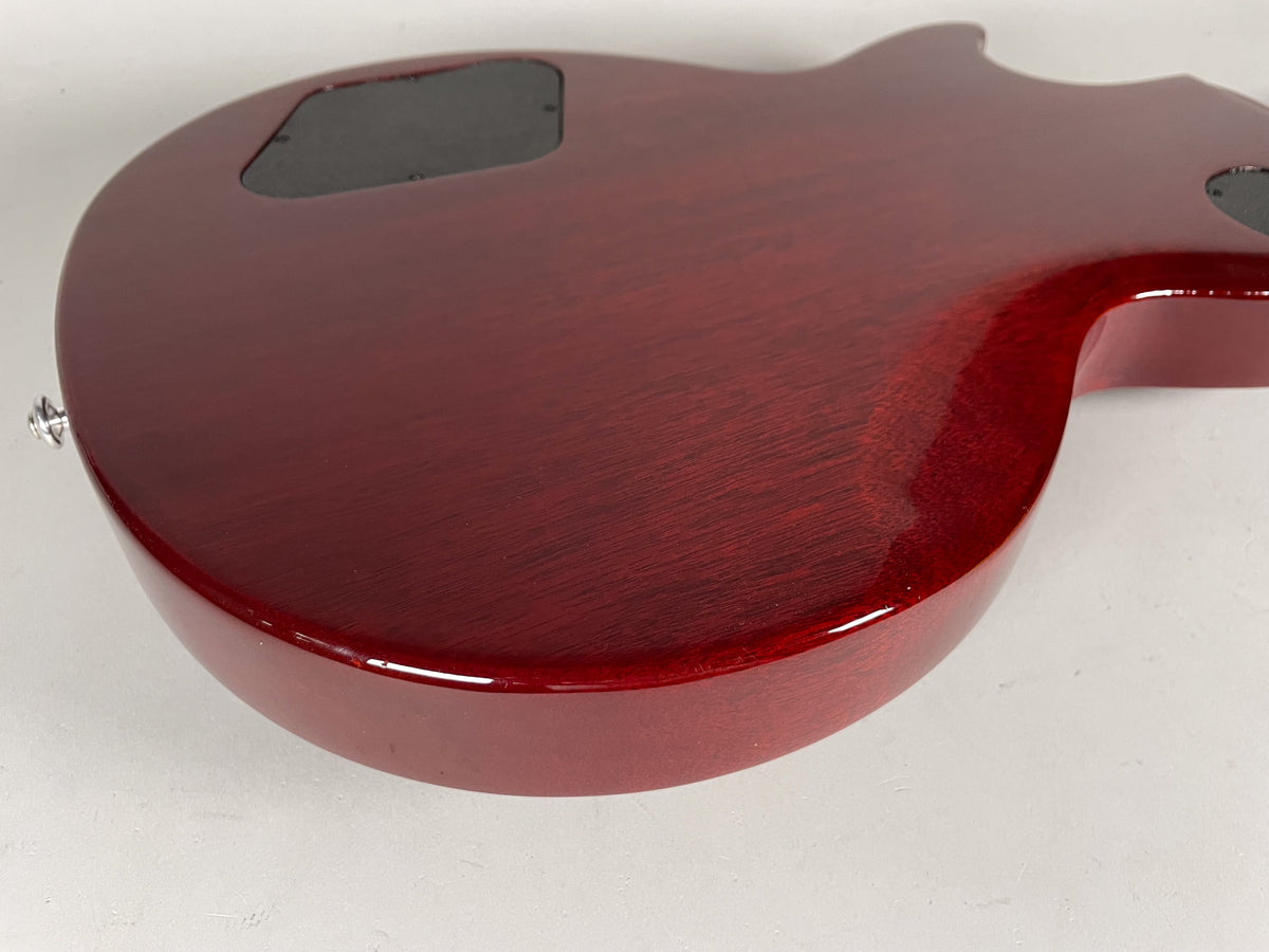 The back of a cherry red guitar body, angled from the lower bout, showing a control cavity cover and a strap button.