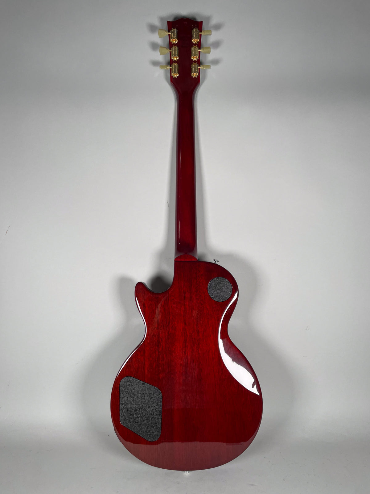 Full rear view of a cherry red Les Paul with a glossy finish, showing gold tuners and two black control cavity covers.