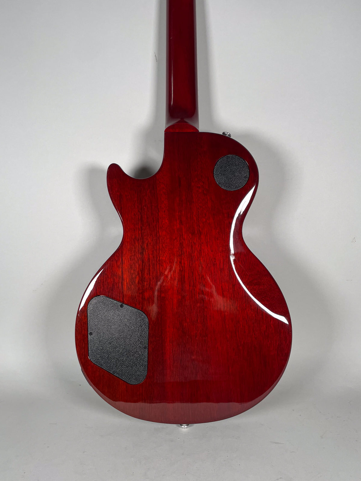 The back of a cherry red electric guitar, showing the glossy finish, two black control cavity covers, and a strap button.