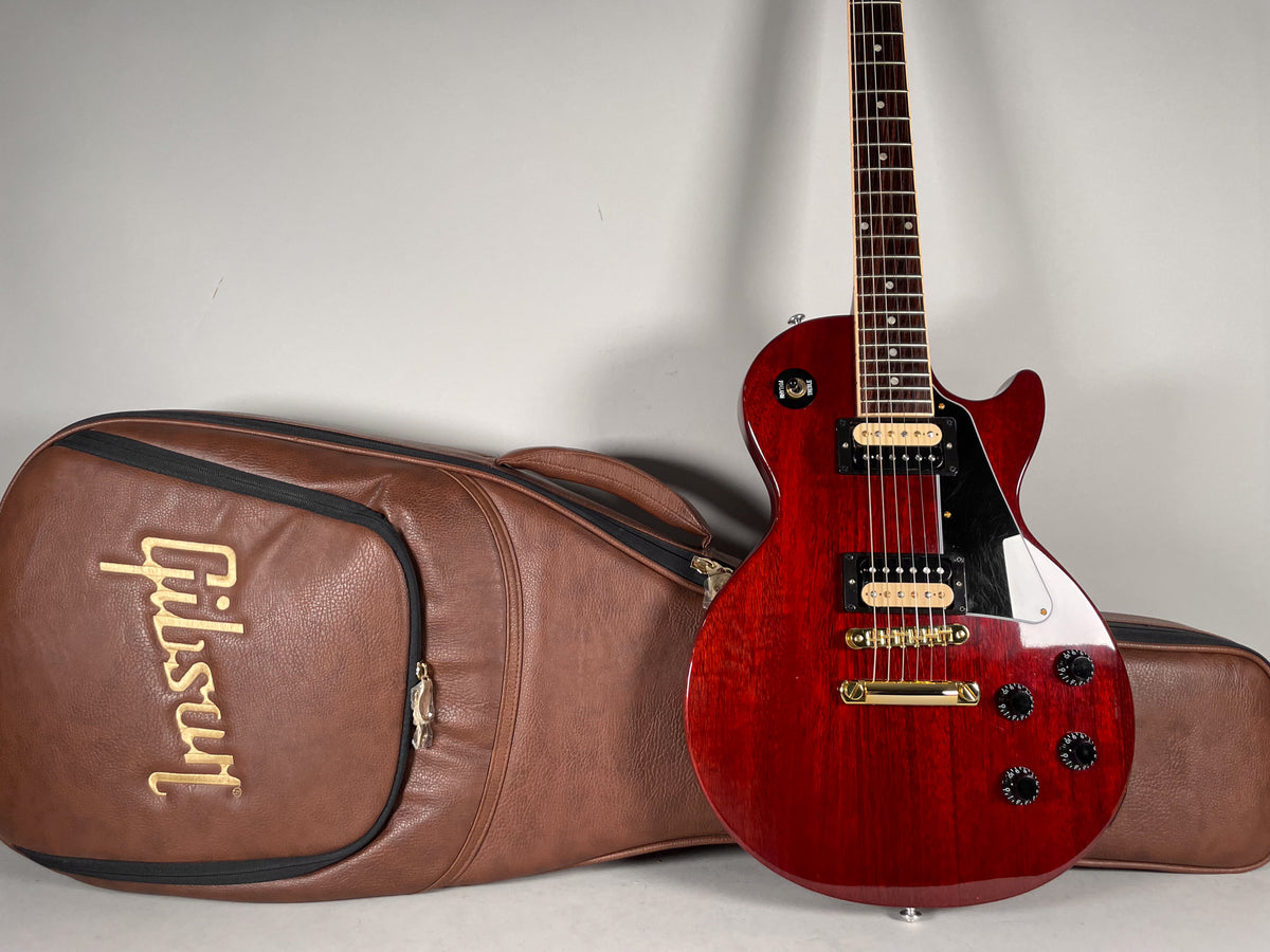 Full view of a cherry red Les Paul Special with a black pickguard, gold hardware, and a brown soft case.