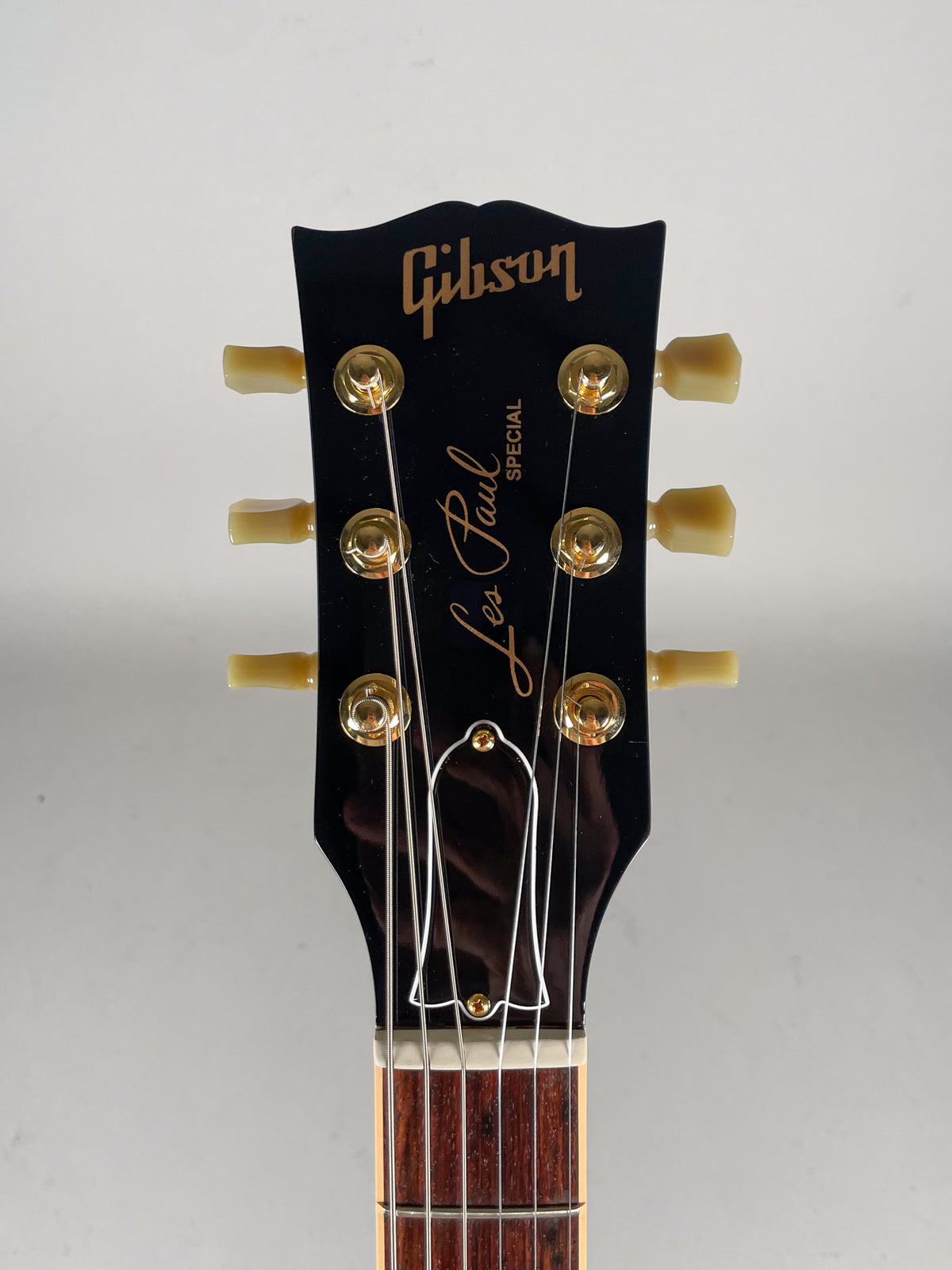 The black headstock, with gold tuners and cream buttons, is centered, showing the top of the fretboard and nut.