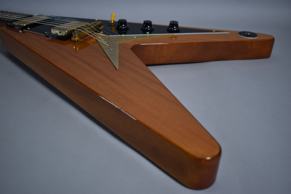 Close-up of the natural finish Flying V body, showing the V-shaped tailpiece, black pickguard, and four black control knobs.