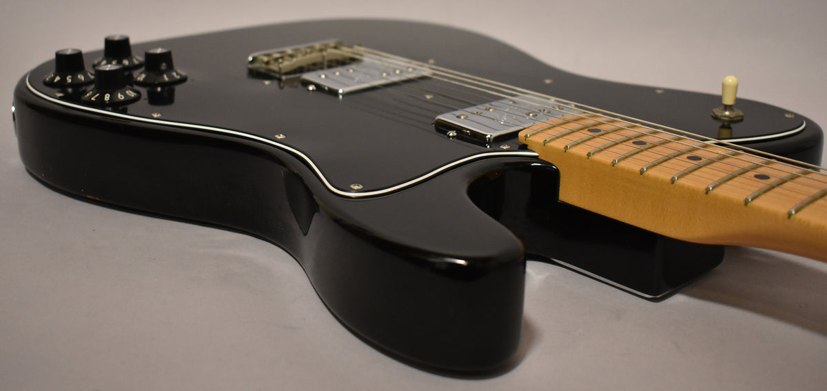 Black Telecaster Deluxe, angled from the lower bout, showing four black numbered control knobs, two chrome humbuckers, and a maple neck.