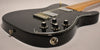 Close-up of the black guitar body, showing four numbered black control knobs, chrome bridge, and output jack.