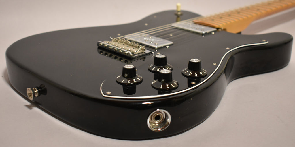 Close-up of the black guitar body, showing four numbered black control knobs, chrome bridge, and output jack.