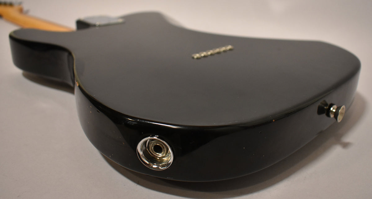 The black guitar's body is angled from the back, showing the input jack, strap button, and string-through-body ferrules.
