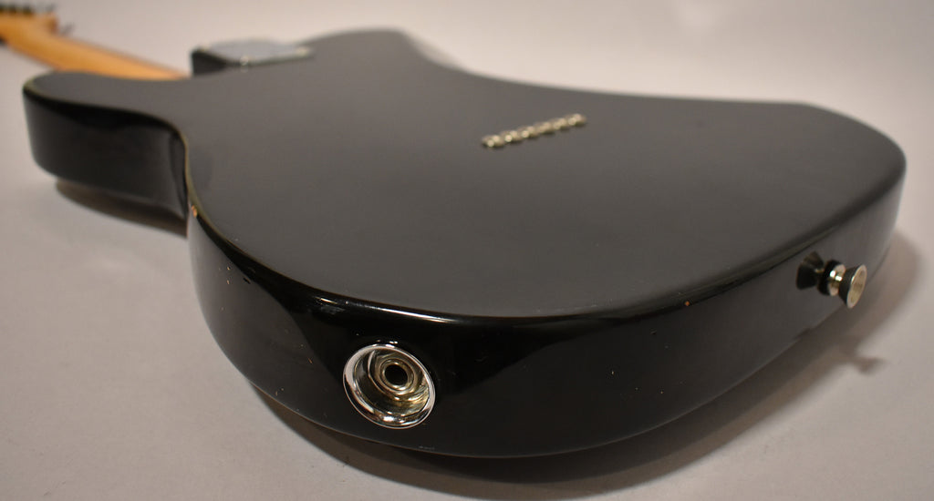 The black guitar's body is angled from the back, showing the input jack, strap button, and string-through-body ferrules.