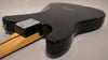 The black guitar body is seen from the back, angled right, showing the neck plate, output jack, and a small chip on the upper bout.