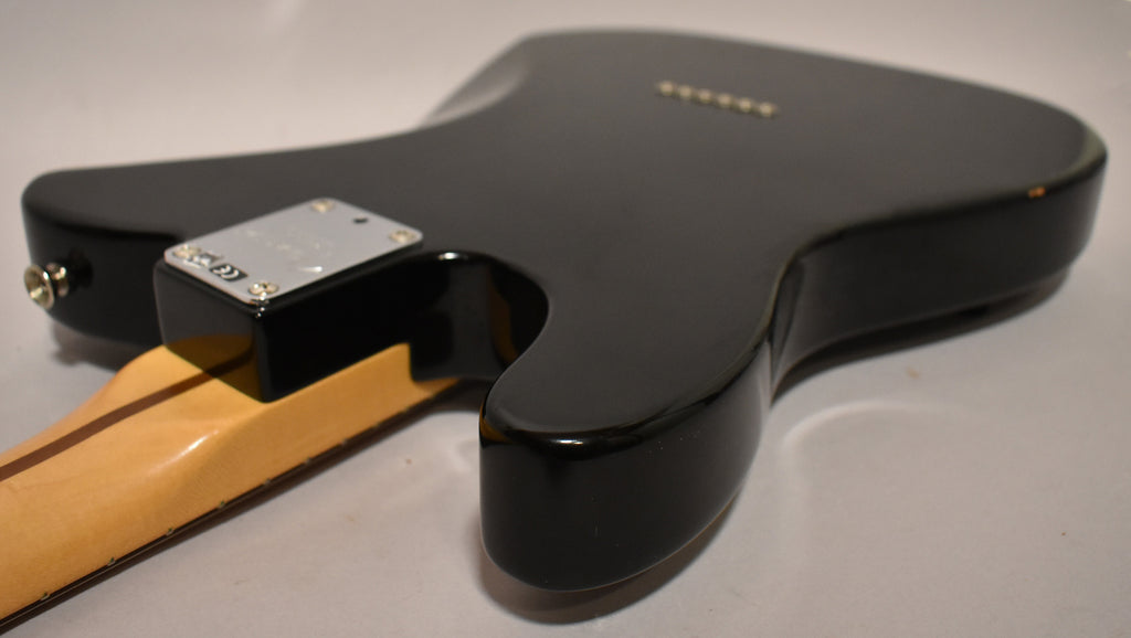 The black guitar body is seen from the back, angled right, showing the neck plate, output jack, and a small chip on the upper bout.