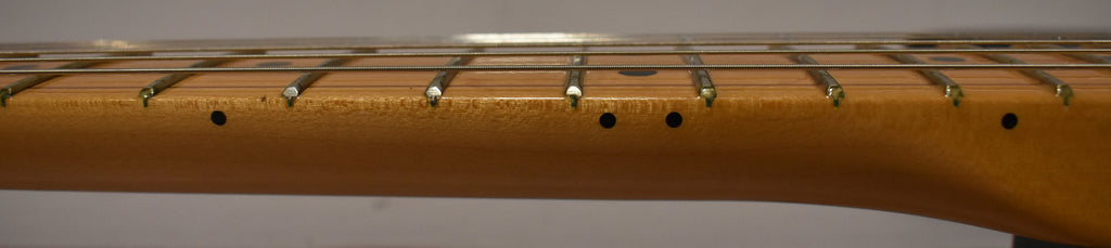 Close-up of the maple fretboard and frets, showing black dot inlays and some light wear along the lower edge.