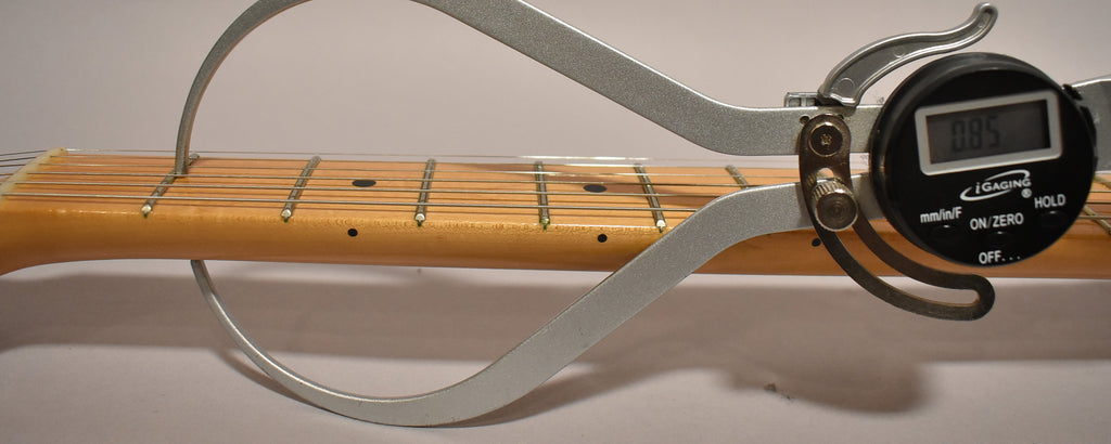 A digital caliper measures the fret height of the maple fretboard, showing 0.85mm, with light wear visible on the frets.