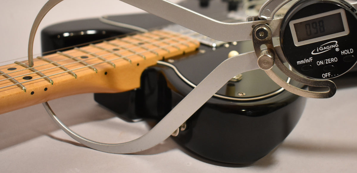 A digital fret height gauge measures the black guitar's maple neck and fretboard, showing a reading of 0.98.